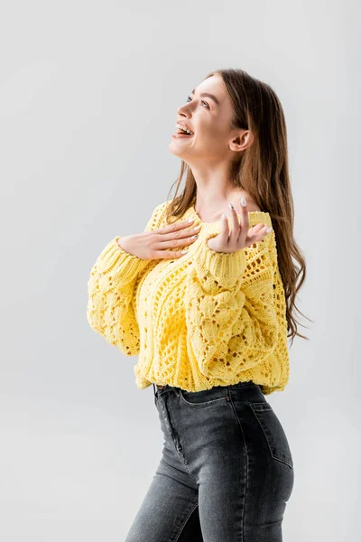 Excited girl in yellow sweater laughing and holding hand on chest isolated on grey — Stock Photo