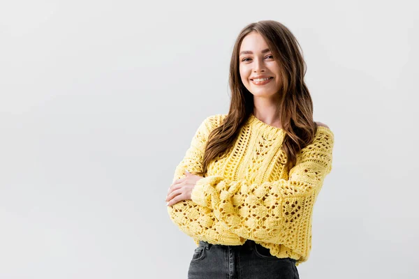 Smiling girl looking at camera while standing with crossed arms isolated on grey — Stock Photo