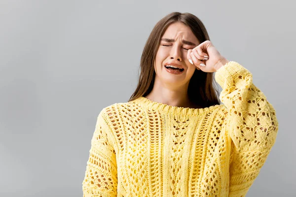 Beleidigtes Mädchen in gelbem Pullover weint und wischt Tränen mit der Hand isoliert auf grau — Stockfoto
