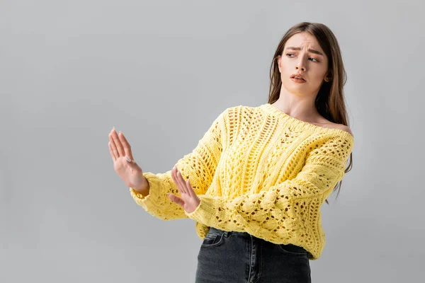 Chica disgustada en suéter amarillo mostrando gesto de stop mientras mira hacia otro lado aislado en gris - foto de stock