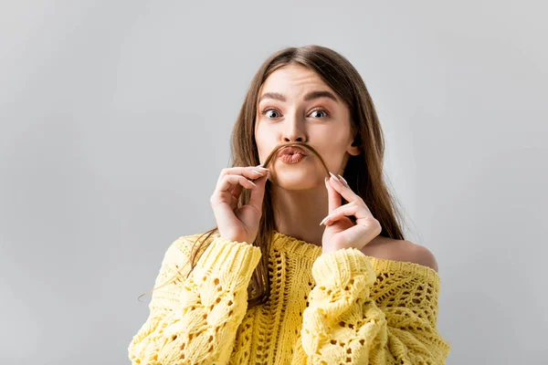 Tricky girl in yellow sweater holding hair above lip like mustache isolated on grey — Stock Photo