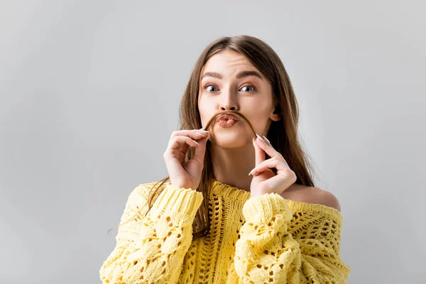 Ragazza ingannevole in maglione giallo tenendo i capelli sopra il labbro come baffi isolati su grigio — Foto stock