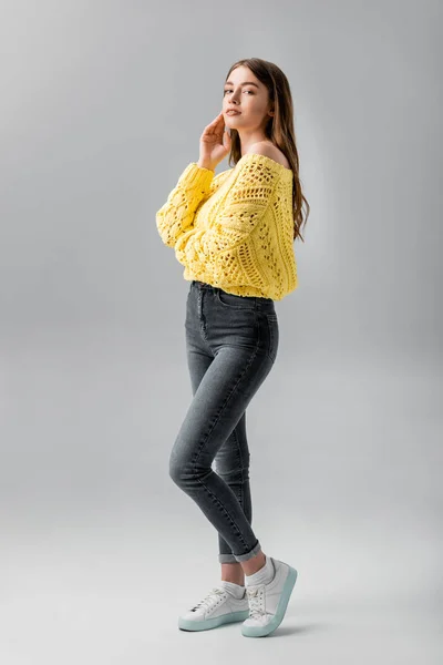 Atractiva, chica coqueta mirando a la cámara mientras toca la cara en el fondo gris — Stock Photo