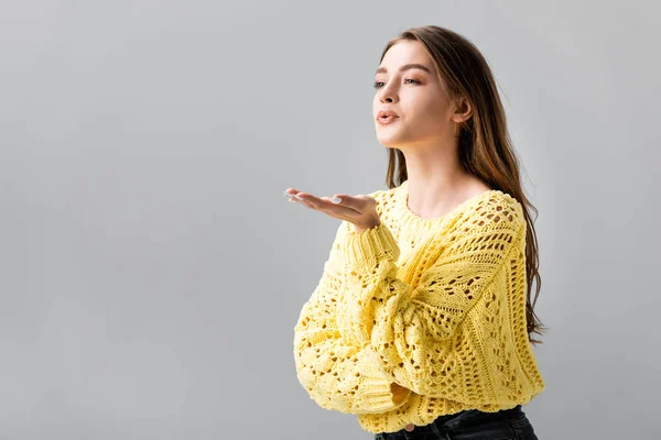 Pretty girl in yellow sweater showing blowing kiss isolated on grey — Stock Photo
