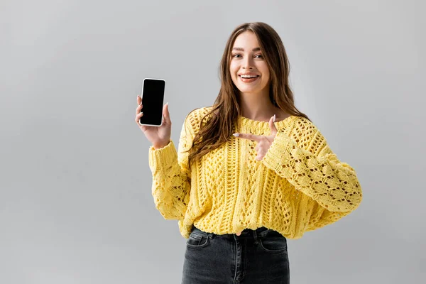Cheerful young woman pointing with finger at smartphone with black screen isolated on grey — Stock Photo