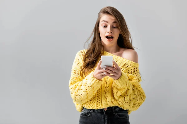 Surprised girl in yellow sweater using smartphone isolated on grey — Stock Photo