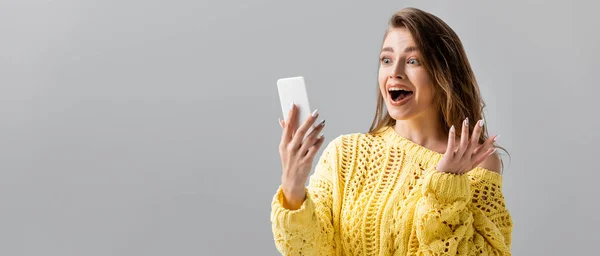 Tiro panorâmico de menina chocada mostrando gesto wow durante bate-papo por vídeo no smartphone isolado em cinza — Fotografia de Stock