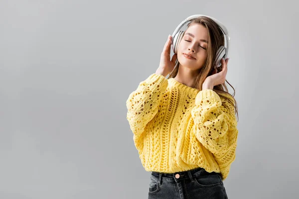 Lächelndes Mädchen tanzt, während es Musik in drahtlosen Kopfhörern hört, mit geschlossenen Augen isoliert auf grau — Stockfoto