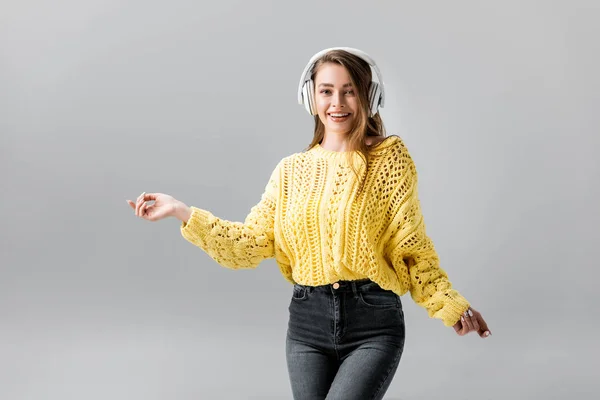 Cheerful girl listening music in wireless headphones and dancing isolated on grey — Stock Photo