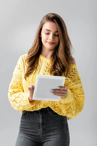 Smiling girl in yellow sweater using digital tablet isolated on grey — Stock Photo