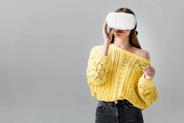 Mujer joven en suéter amarillo con auriculares vr aislados en gris - foto de stock