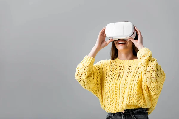 Fille gaie en pull jaune en utilisant un casque de réalité virtuelle isolé sur gris — Photo de stock