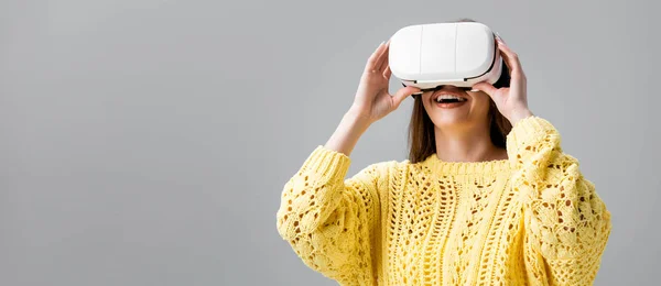 Панорамный снимок веселой девушки с помощью гарнитуры виртуальной реальности, изолированной на сером — стоковое фото