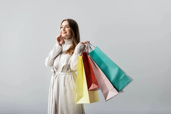 Ragazza alla moda guardando altrove mentre tiene borse della spesa isolate sul grigio — Foto stock