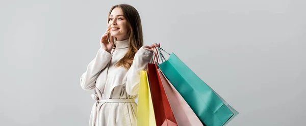 Colpo panoramico di ragazza alla moda guardando lontano mentre tiene borse della spesa isolate sul grigio — Foto stock