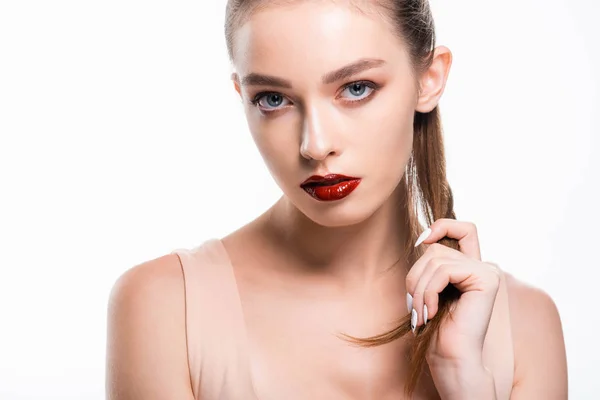 Atractiva mujer joven mirando a la cámara y tocando el cabello aislado en blanco — Stock Photo