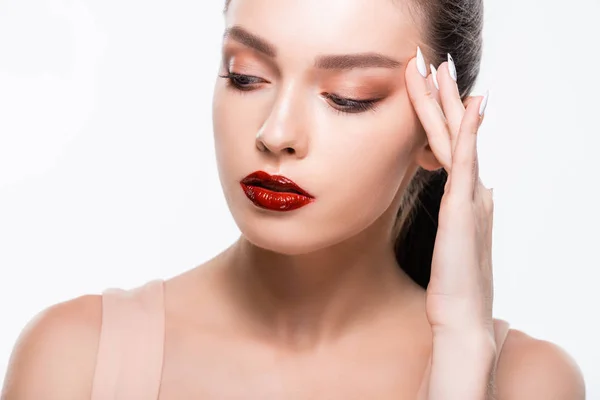 Chica atractiva con labios rojos y maquillaje tocando la cara aislado en blanco - foto de stock