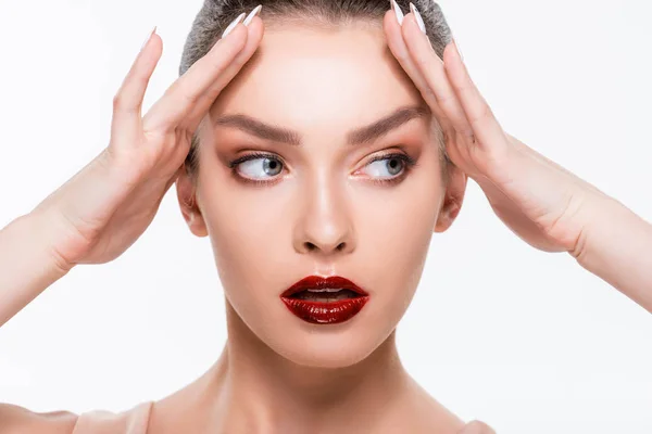 Atractiva chica con labios rojos tocando la frente mientras mira hacia otro lado aislado en blanco — Stock Photo