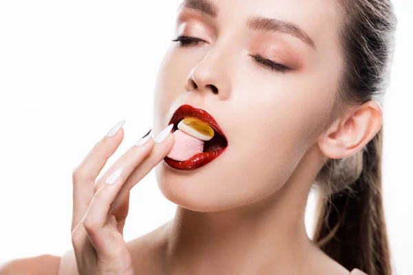 Beautiful young woman with red lips and makeup eating candies isolated on white — Stock Photo