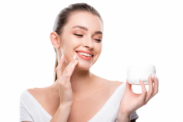 Hermosa, chica sonriente aplicando crema cosmética en la cara aislada en blanco - foto de stock