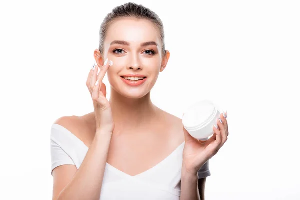 Attractive, smiling woman applying face cream and looking at camera isolated on white — Stock Photo