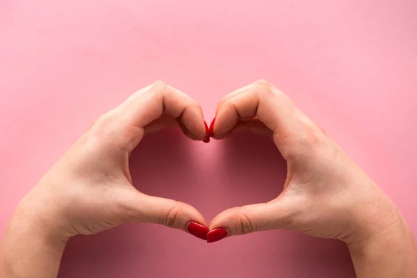 Cropped view of woman showing heart-shaped sign with hands on pink — Stock Photo