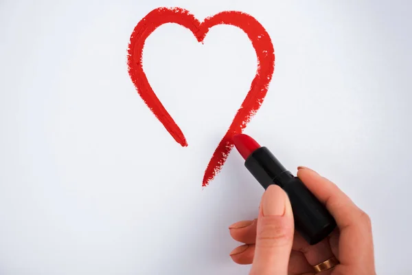 Vista recortada de la mujer dibujando corazón mientras sostiene lápiz labial rojo aislado en blanco - foto de stock