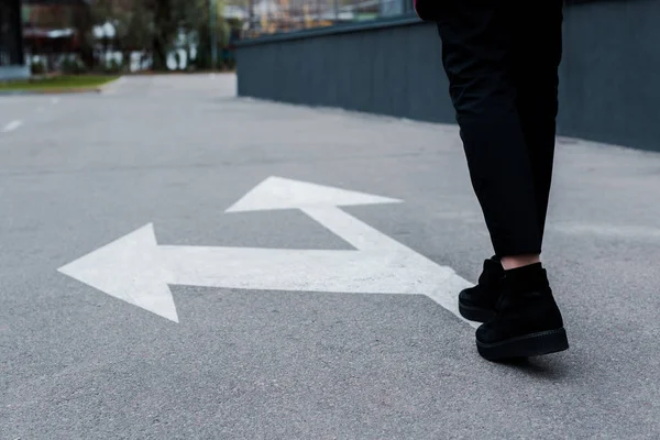 Cropped view of woman walking near directional arrows on asphalt — Stock Photo