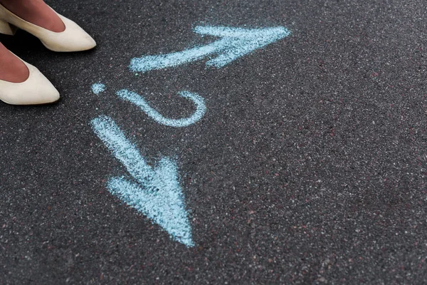 Vista ritagliata della donna in piedi vicino frecce direzionali e punto interrogativo su asfalto — Foto stock