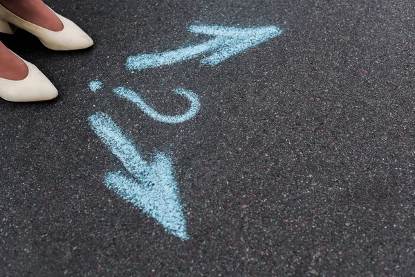 Vue recadrée de la femme debout près des flèches directionnelles et point d'interrogation sur l'asphalte — Photo de stock