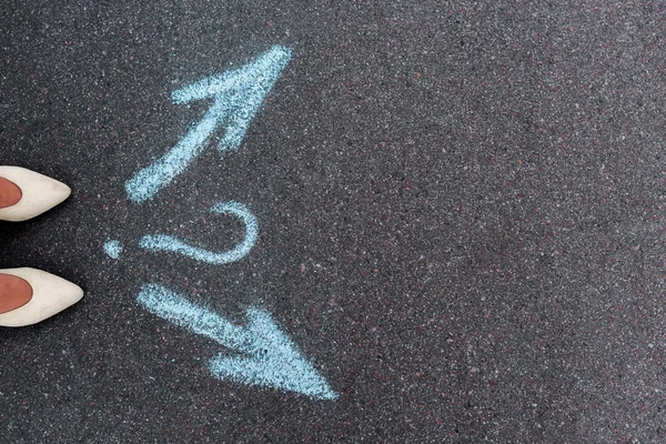 Top view of woman standing near directional arrows and question mark on asphalt — Stock Photo