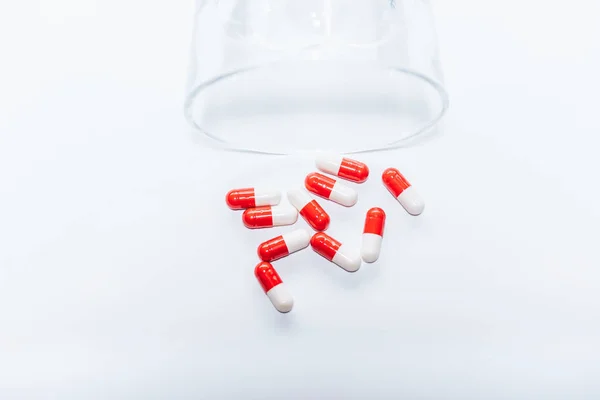 Rote und weiße Kapseln in der Nähe von umgekipptem Glas auf weißem Hintergrund, Suizidpräventionskonzept — Stockfoto