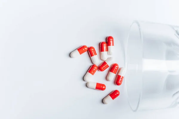 Red and white capsules near overturned glass on white background, suicide prevention concept — Stock Photo