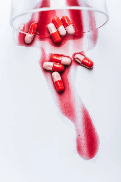 Vidrio volcado y píldoras mojadas en derrames rojos de agua sobre fondo blanco, concepto de prevención del suicidio - foto de stock