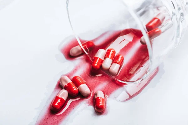 Overturned glass and wet pills in red spills of water on white background, suicide prevention concept — Stock Photo