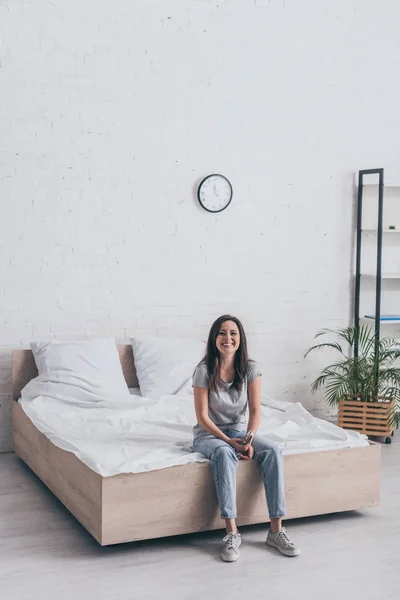 Fröhliche junge Frau sitzt im Schlafzimmer und lächelt in die Kamera — Stockfoto