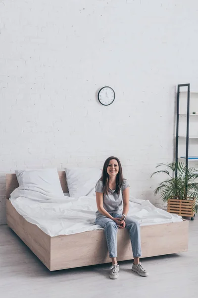 Joyeuse jeune femme assise dans la chambre et souriant à la caméra — Photo de stock