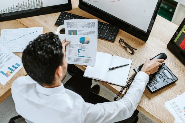 Overhead view of bi-racial trader looking at paper and holding handset — Stock Photo