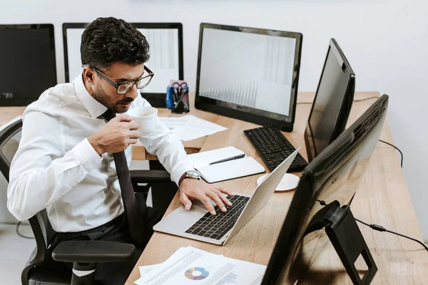 High angle view of bi-racial trader drinking coffee and using laptop — Stock Photo