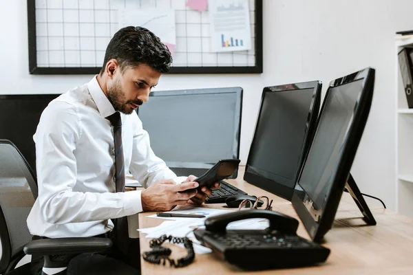 Trader bi-racial comptant avec calculatrice et assis à table — Photo de stock