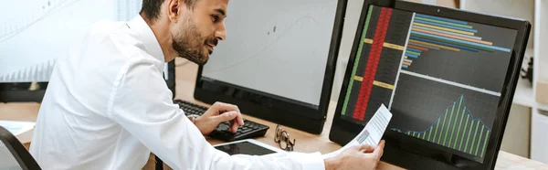 Panoramic shot of smiling bi-racial trader looking at paper — Stock Photo