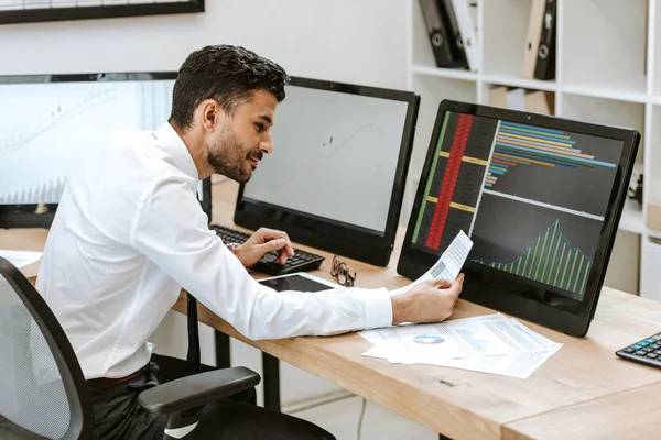 Side view of smiling bi-racial trader looking at paper — Stock Photo