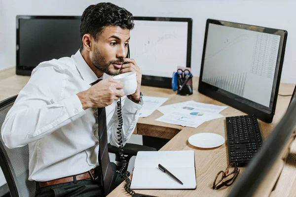 Bi-racial trader talking on telephone and holding cup of coffee — Stock Photo