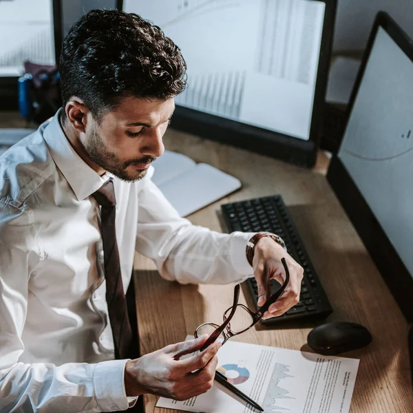 Hochwinkel-Ansicht von bi-rassischen Händlern, die Papier betrachten und in der Nähe von Computern mit Grafiken sitzen — Stockfoto