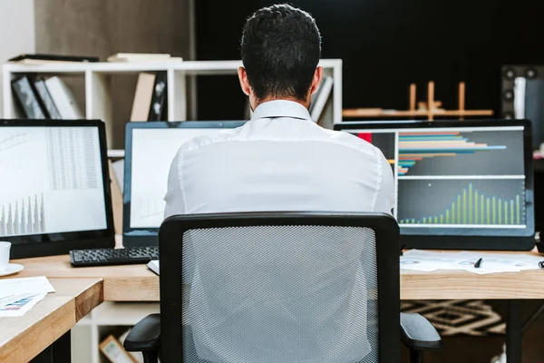 Rückseite des bi-rassischen Händlers, der Computer mit Graphen betrachtet — Stockfoto