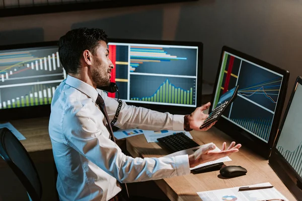High angle view of bi-racial trader talking on telephone and looking at computer with graphs — Stock Photo