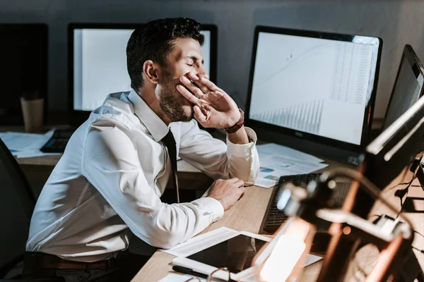 Bi-racial trader yawning and sitting near computer with graphs — Stock Photo