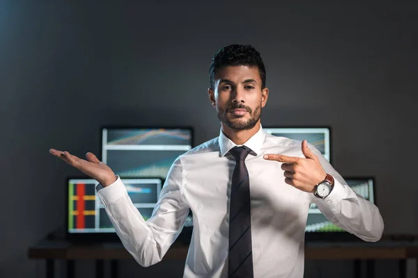 Zweirassiger Händler, der mit dem Finger zeigt und Computer mit Graphen auf dem Hintergrund — Stockfoto