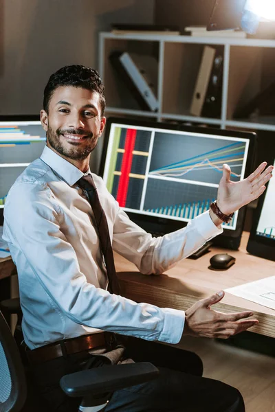 Sonriente bi-racial comerciante con la mano extendida mirando a la cámara - foto de stock