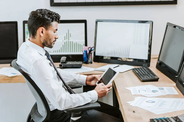 Seitenansicht von bi-racial Trader mit digitalem Tablet und sitzen in der Nähe von Computern mit Grafiken — Stockfoto